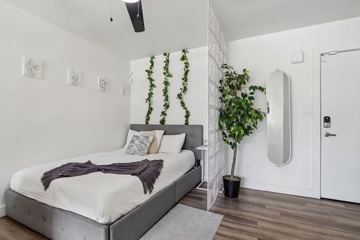 Modern bedroom with sleek gray bed, decorative wall greenery, and elegant full-length mirror, creating a tranquil and stylish retreat.