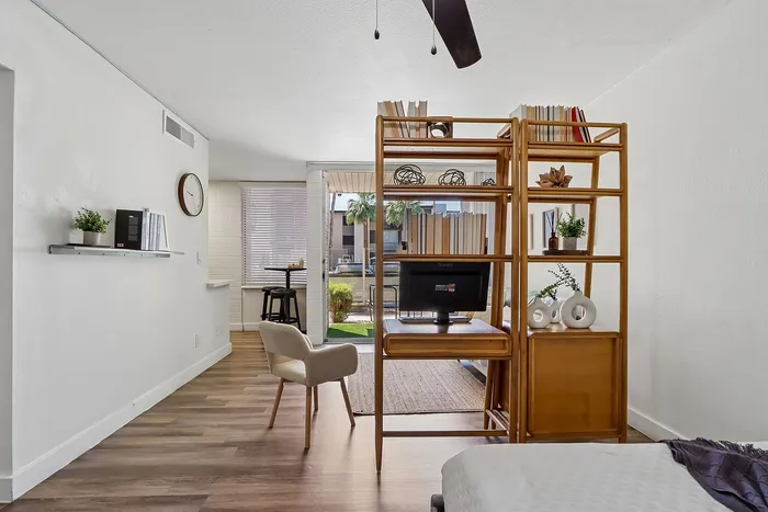 Modern apartment interior featuring an open-concept layout with elegant wooden shelving, cozy chair, and stylish decor, overlooking a sunny patio.