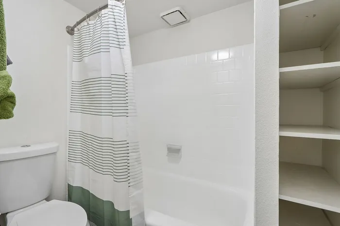 Elegant bathroom with pristine white tiles, modern shower curtain, and handy built-in shelving.