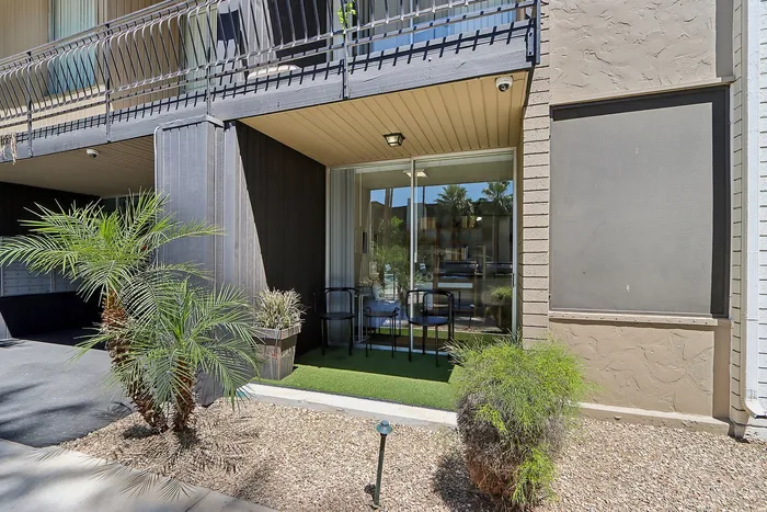 Charming apartment entry with a cozy patio space, featuring sleek black chairs and lush greenery, creating an inviting outdoor retreat.