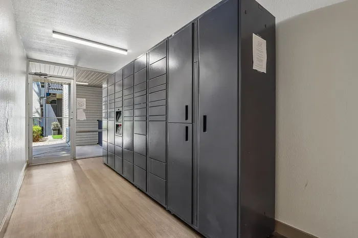 Contemporary apartment hallway featuring sleek, secure package lockers and natural light from a glass exit door.