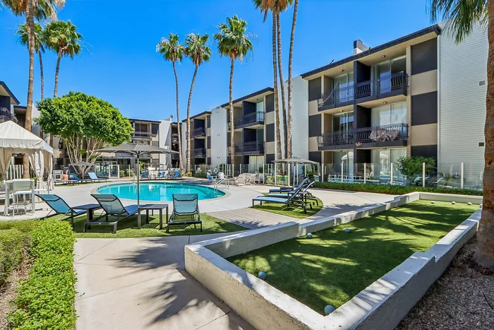 Beautiful apartment complex with a sparkling pool, surrounded by lush palm trees and modern sun loungers, offering a luxurious outdoor leisure area.