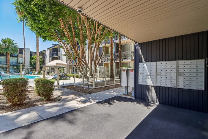 Charming apartment complex courtyard featuring a sparkling pool, lush greenery, and modern architecture with convenient mailbox access.