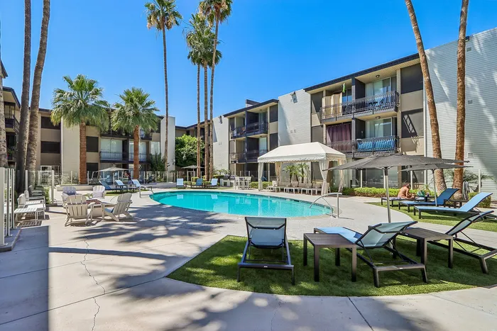 Luxurious apartment complex with a sparkling pool surrounded by elegant lounge chairs and lush palm trees.