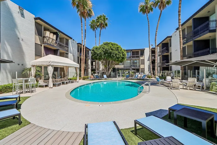 Inviting outdoor pool area with lush palm trees, cozy lounge seating, and a stylish cabana, perfect for relaxation at a modern apartment complex.