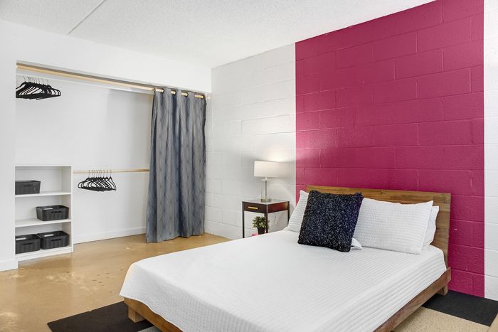 Chic bedroom featuring a cozy bed with crisp white linens, a striking pink accent wall, and a spacious built-in closet with open shelving.