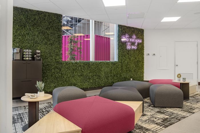 Trendy lounge area with vibrant pink and gray seating, lush green wall, and neon sign for a stylish, modern ambiance.