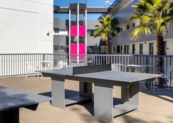 Vibrant outdoor courtyard featuring a sleek ping pong table and stylish patio seating, surrounded by modern architectural design and tropical palm trees.
