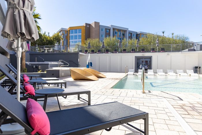Inviting outdoor pool area with stylish loungers and modern apartment building backdrop, perfect for relaxation and enjoyment.