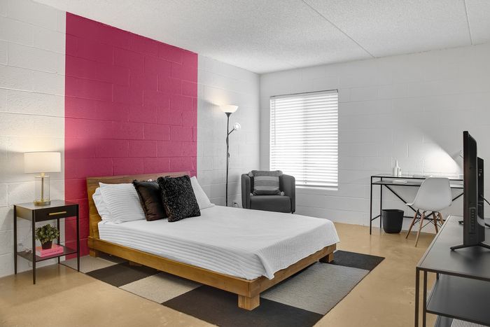 Modern bedroom with stylish pink accent wall, featuring a cozy bed, elegant desk, and ample natural light.