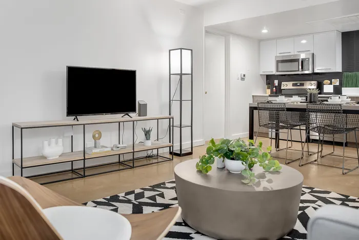 Modern living room with sleek decor, featuring a cozy seating area, flat-screen TV, and an open kitchen with a stylish breakfast bar.