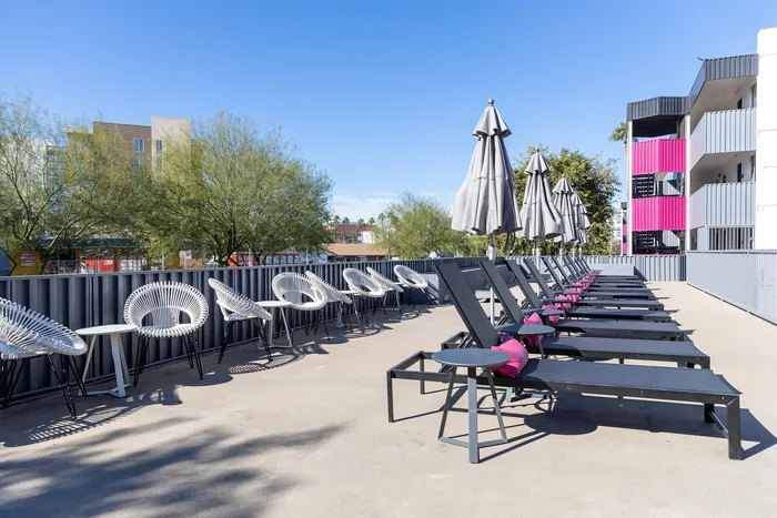 Modern outdoor seating area with sleek lounge chairs, vibrant accents, and parasols, ideal for relaxation under a clear blue sky.