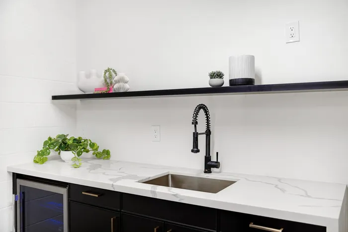 Sleek modern kitchen area with elegant marble countertop, stylish black cabinetry, and chic floating shelf decor.