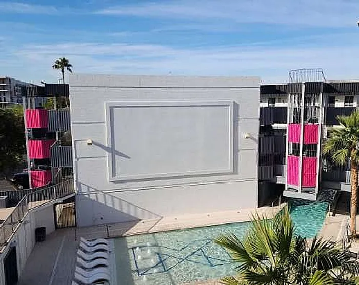 Vibrant apartment complex with a striking exterior, featuring a large pool and sunny lounge area, perfect for relaxation.