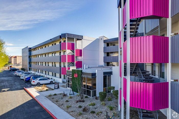 Contemporary apartment complex with vibrant pink accents and ample parking, offering a modern urban living experience.