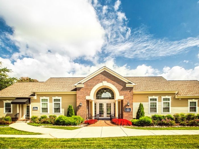 1-Bedroom Apartments in Laurel, MD - SouthRidge Apartments & Townhomes - Leasing Office Entrance With Brick Arch Entry, White Trim Windows, Manicured Landscaping, And Sidewalk Approach.