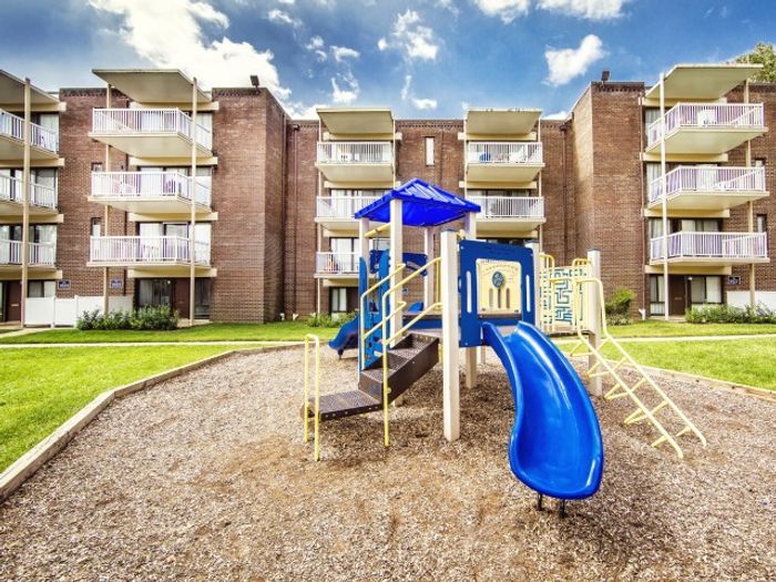 Apartments in Laurel, MD - SouthRidge Apartments & Townhomes - Courtyard Playground With Blue Slide And Climbing Structure In Front Of Brick Apartment Buildings With Balconies And Green Lawn.
