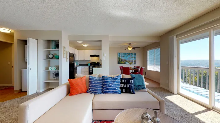 Dog-Friendly Apartments in Renton, WA - Sunset View Apartments - Open Concept Living Room With Carpet Flooring, Sectional Sofa, Red Accent Chair, Patterned Rug, And Sliding Glass Doors To Balcony.
