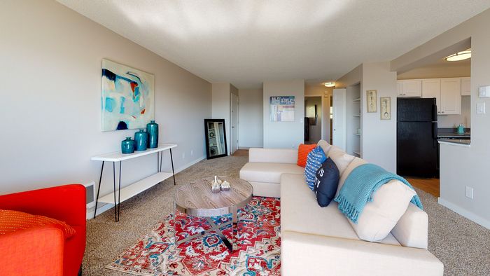 Renton WA Apartments for Rent - Sunset View - Carpet, Nude Sectional Couch, Wooden Circle Coffee Table, Blue, and Red Area Rug, and Mult-Colored Decorative Pillows