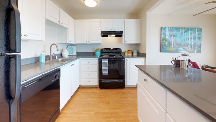 Renton, WA, Apartments - Sunset View Apartments - Bright Kitchen With White Cabinets, Gray Countertops, Black Appliances, And Breakfast Island Overlooking Dining Area.