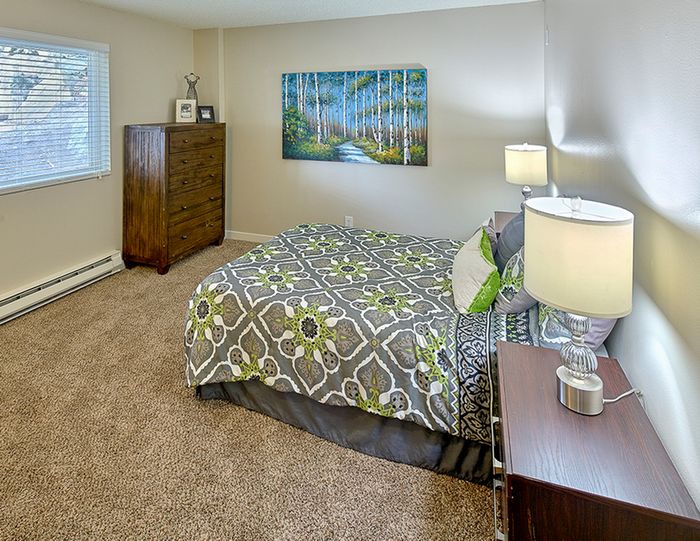 1-Bedroom Apartments in Renton, WA - Sunset View Apartments - Cozy Bedroom With Plush Carpet, Nightstands With Lamps, Wooden Dresser, And Large Window With Blinds.