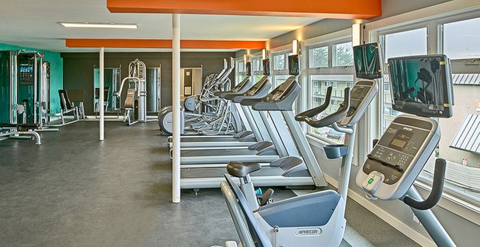 One-Bedroom Apartments in Renton, WA - Sunset View Apartments - Modern Fitness Center With Stationary Bike, Treadmills, Elliptical Machines, Weight Training Equipment, And Large Windows.