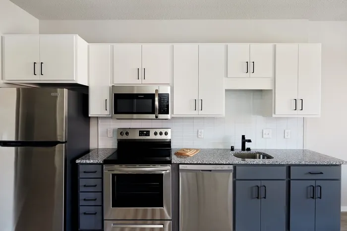 Dog-Friendly Apartments in Minneapolis, MN - B-Side - A Two-Bedroom Kitchen With White Cabinets, Blue-Base Cabinets, Quartz Countertops, and Stainless Steel Appliances.