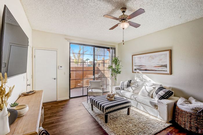 North Las Vegas, NV, Studios for Rent - Desert Ridge Apartments - Living Room With Sofa, Ceiling Fan, Coffee Table, and Glass Windows Overlooking the Private Patio and Outdoor View.