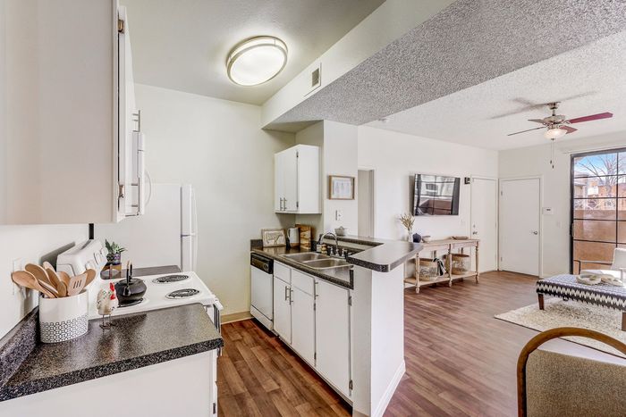 KitchenStudio Apartments in North Las Vegas, NV - Desert Ridge Apartments - Open Kitchen With Breakfast Bar, Granite Countertops, White Cabinets, Electric Stove, and Wood Flooring.