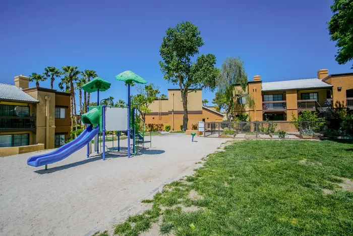 Playground Dog-Friendly Apartments in North Las Vegas, NV - Desert Ridge Apartments - Playground With Slide, Shade Canopies, Open Lawn, and Apartment Homes Nearby.