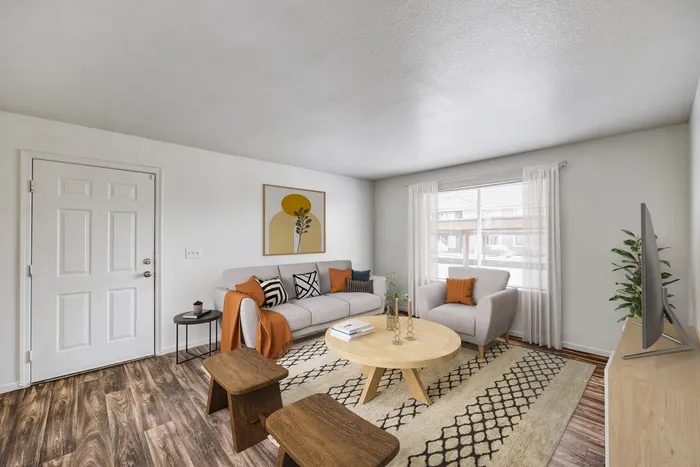 Apartments for Rent in West Las Vegas - Portola Del Sol - Living Room Area with Neutral Color Couch, Large Circle Coffee Table, Short Round Stools, Wood-Style Flooring, and a Large Window