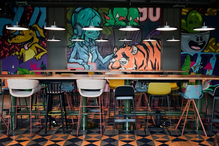 Minneapolis, MN, Apartments With In-Unit Washer and Dryer - B-Side - Co-Working Lounge With Long Communal Table, Mixed Seating, Pendant Lights, and Bold Wall Mural With Vibrant Colors.