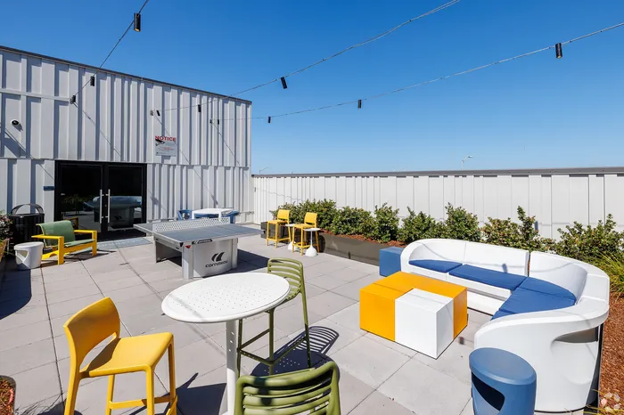 West Oakland, CA, Apartments with In-Unit Washer and Dryer - Prescott Station - Rooftop Features Colorful Outdoor Seating, Round Tables, String Lights Overhead, And A Ping Pong Table.