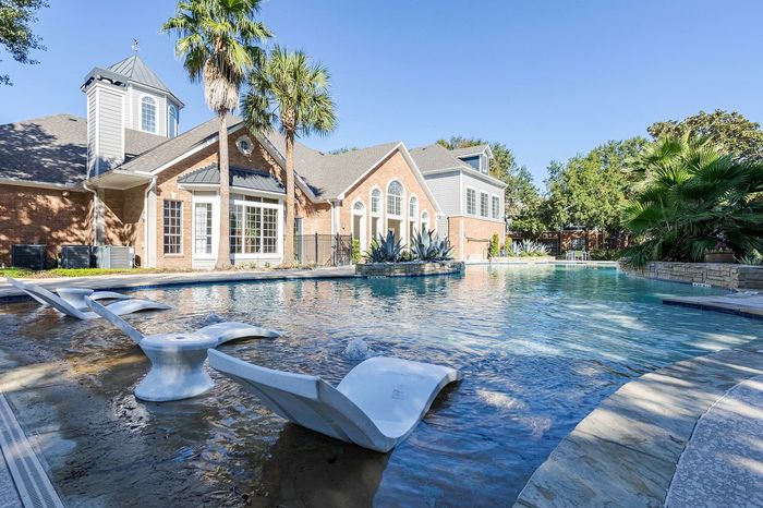 Westchase, TX, Apartments Near Westpark Tollway - Gramercy Park - A Resort Style Swimming Pool With Clear Blue Water, Stone Decking, And Palm Trees.