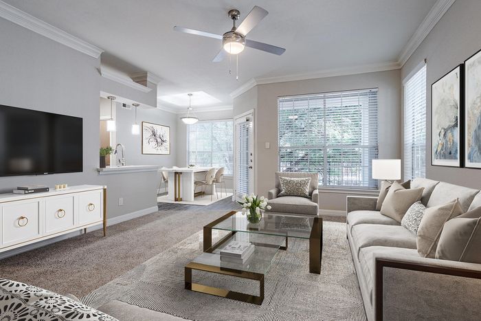Apartments in Westchase, TX, with In-Unit Washer and Dryer - Gramercy Park - A Living Room With Gray Sofa, Glass Coffee Table, Wall-Mounted Television, Ceiling Fan, And Large Windows.