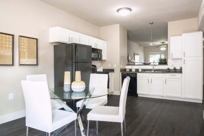 North Austin, TX, Pet-Friendly Apartments - Lotus Village Apartments - A Kitchen With White Cabinets, Black Appliances, Glass Table, And Modern Pendant Lighting.