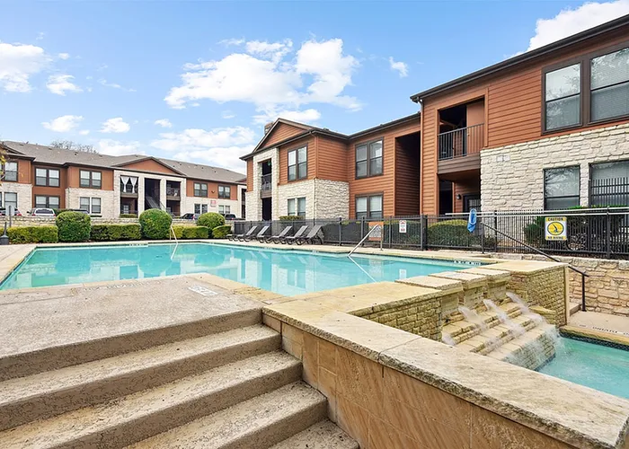 South Austin, TX, Apartments Near Downtown Austin - Saratoga Ridge - Resort Style Pool With Stone Steps, Lounge Chairs, And Shaded Pergola Seating Surrounded By Mature Trees.