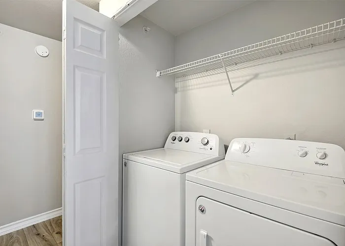 South Austin, TX, Apartments Near Bluff Springs - Saratoga Ridge - In-Home Laundry Closet With Full-Size Washer And Dryer, White Shelving, And Easy Access Doorway.