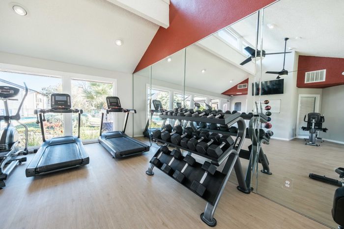 2-Bedroom Apartments in Austin, TX - Agave Falls - Fitness Center Featuring Wood-Style Flooring, Wall Mirrors, Free Weights, Treadmills, and Large Windows.