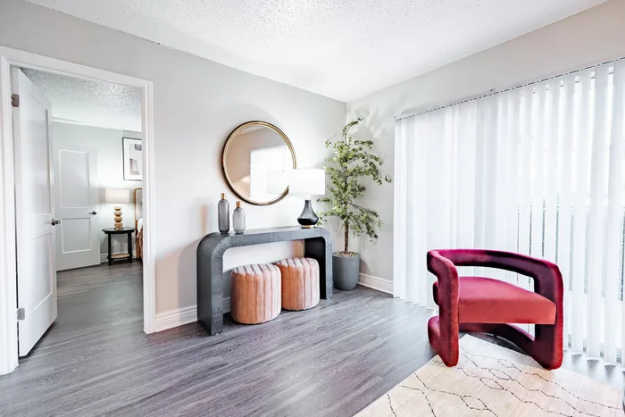 Irving, TX, Apartments Near DFW Airport - Bridgeport Apartment Homes - Bright Living Room with Sofa, Round Coffee Table, Wood Flooring, Floor Lamp, and Sliding Glass Door with White Curtains.