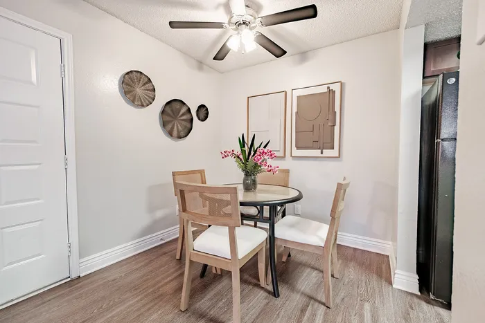 Irving, TX, Apartments Near Toyota Music Factory - Bridgeport Apartment Homes - Dining Room with Round Table, Dining Chairs, Wall Decor, Ceiling Fan Light, and Wood Flooring.