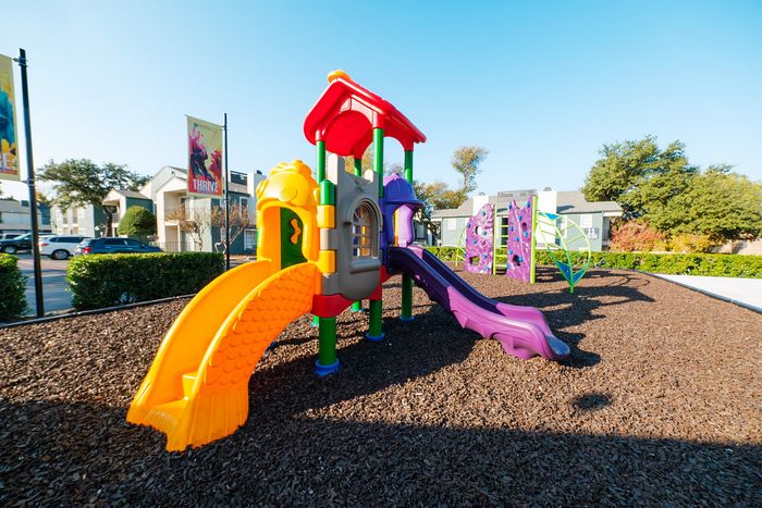 North Dallas, TX, Apartments Near DART - Ventana Apartment Homes - A Colorful Outdoor Playground Features Bright Slides, Climbing Structures, And Wood-Chip Ground.