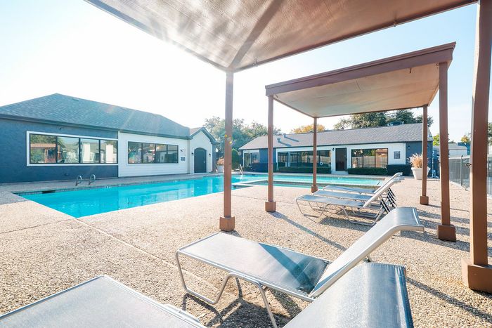 North Dallas, TX, Apartments Near Dallas North Tollway - Ventana Apartment Homes - A Swimming Pool Features Lounge Chairs and Cabanas Under A Large Pergola, Modern Buildings, And A Concrete Deck.