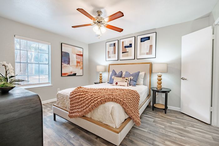 North Dallas, TX, Pet-Friendly Apartments - Ventana Apartment Homes - A Bedroom With A Peach Knit Throw Blanket, Blue Pillows, Black Side Tables, Lamps, Art Decor, And A Large Window With Blinds.