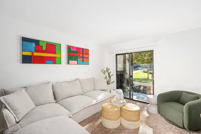 One-Bedroom Apartments in Palatine, IL - The Clayson - A Living Room With A Large Sectional Sofa, Colorful Wall Art, Woven Ottomans, And Sliding Glass Door To Patio.