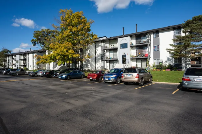 West Chicago, IL, Pet-Friendly Apartments - Timber Lake Apartment Homes - A Large Parking Lot Full Of Cars, Green Lawn, Mature Trees With Fall Leaves, And Multi-Story Balconies.