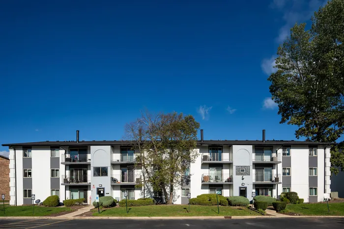 One-Bedroom Apartments in West Chicago, IL - Timber Lake Apartment Homes - Exterior View of The Apartment Building With Multiple Balconies, Landscaped Shrubs, And Central Walkways.