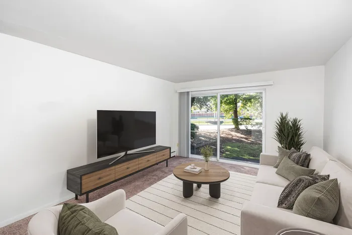 Justice, IL, Apartments Near Downtown Chicago - Willow Hill Apartments - Modern Living Room With Couch, Armchair, Media Console, Flat-Screen Television, Round Coffee Table, and Sliding Glass Doors.