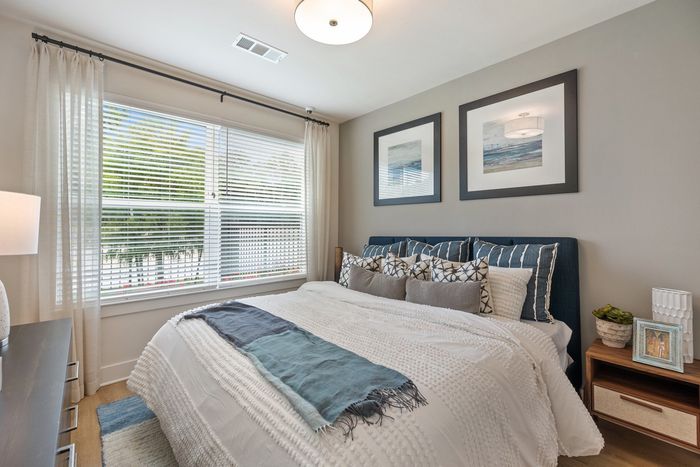 Apartments in Houston, TX, with In-Unit Washer and Dryer - Acova Brentwood - Bedroom With Large Window, Upholstered Bed, Layered Bedding, Wood-Style Plank Flooring, Wall Art, And Bedside Table.