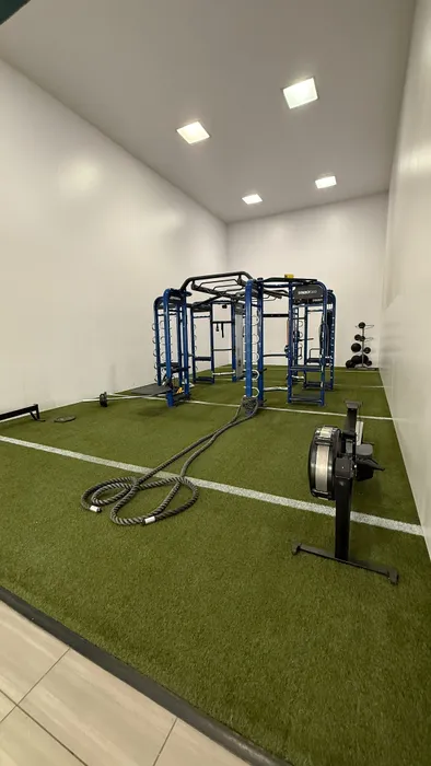 Modern gym with high-tech equipment, featuring a synergy training station and battle ropes on artificial turf.